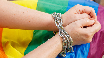 Female hands chained against the background of the LGBT flag. The concept of the fight for tolerance and equal treatment of sexual minorities