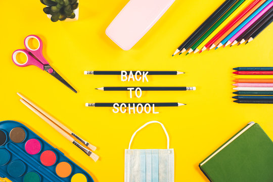 Colorful Flat Lay Background With Craft Supplies.View From Above Of School Accessories On A Yellow Background With Back To School Message.Notebook, Medical Mask, Scissor, Pencils And Paint On The Desk