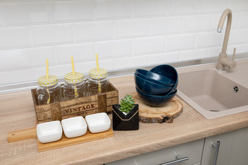Dishes and utensils: plates, saucers on a wooden stand, lemonade jars against the background of a white kitchen.