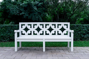 White vintage style bench in the park on green foliage background.