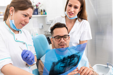 Fototapeta premium Female dentist with an assistant showing dental x-ray of teeth to a male patient in the clinic.