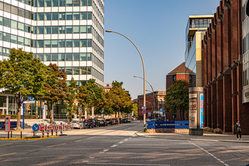 Obraz premium Golden hour cityscape with office building skyscraper and asphalt road. City road and sidewalk in Hamburg business downtown near modern corporate building of futuristic shape