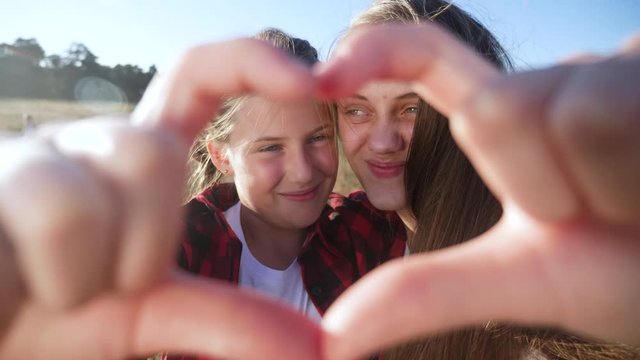happy family in the park. two sisters show a heart symbol with their hands smiling. young mom and daughter show lifestyle heart gesture with fingers. concept people in the park happy family