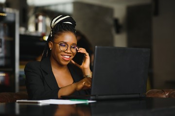 Young beautiful Afro-American businesswoman smart phone and smiling while working in cafe