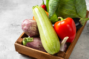 Assortment of vegetables in a wooden box. There are many different raw vegetables in the box. Cabbage, zucchini, garlic, sweet pepper and eggplant on the table. Healthy food concept