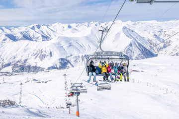 Fototapeta na wymiar Snowboarders sits on the char lift and joyfully poses with Gudauri ski resirt and mountains in the background. Gudauri. Georgia. 28th February, 2020