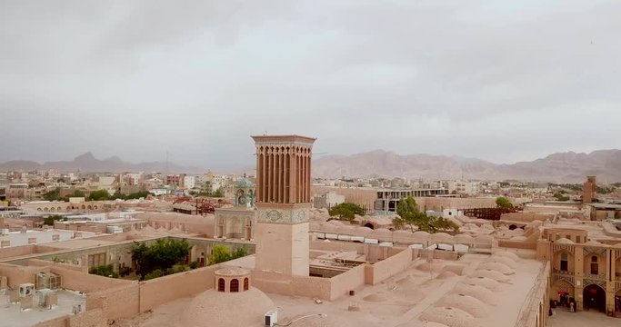 Aerial shot from old windcatcher architecture in Gangali khan, historical city and bazaar in central Kerman city square in Iran in hazy day with mountains landscape