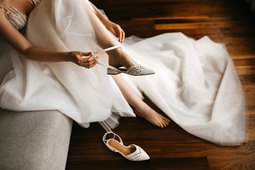 Close-up of a bride in white dress, putting on flat wedding shoes.