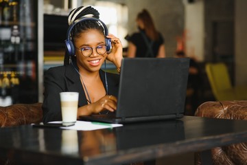 Attractive African American blogger with headphones and laptop communicating with followers in cafe