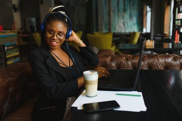 Beautiful Afro American girl in casual clothes is using a laptop and smiling while sitting in cafe