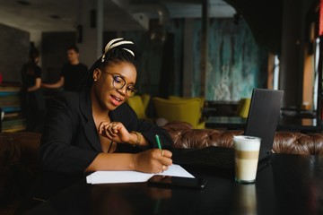 Beautiful Afro American girl in casual clothes is using a laptop and smiling while sitting in cafe