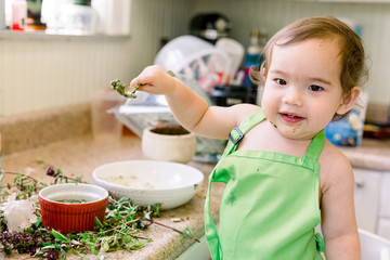 Happy toddler (baby boy) wearing a green apron and holding up a spoon smiling in the kitchen