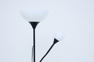 Electric floor lamp in black with white lampshades in the interior of troom against the background of a white wall.