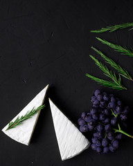 Cheese (brie) on a slate black background with rosemary, grapes flat lay