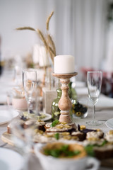 white candle on  wooden candlestick , table is full of food and dishes , selective focus