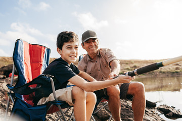Latin grandfather and grandson enjoying day together fishing on the lake. Grandfather helping his...