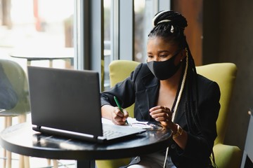 young african american freelancer in medical mask showing thumb down while sitting near laptop in cafe