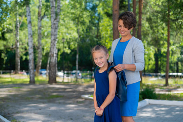 Fototapeta premium A caring mother helps her child put on a backpack. Caucasian woman preparing her daughter for school in the first grade.