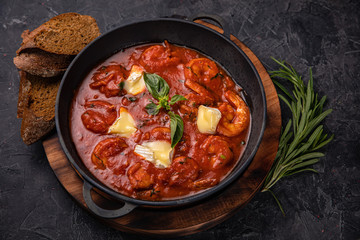 Shrimp and seafood in tomato sauce with herbs on a dark concrete table