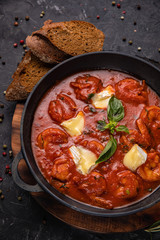 Shrimp and seafood in tomato sauce with herbs on a dark concrete table