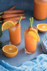 Two glasses of fresh carrot juice and carrots on light blue ground
