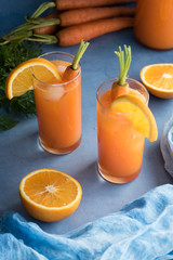 Fresh orange and carrot juice on blue background.
