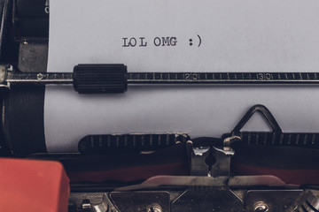 Old vintage retro typewriter, close up. LOL OMG and a smiley text typed words on a white paper...