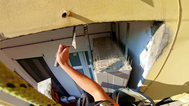 Abseiler workers with rope access and gear at building site, applying cement at home