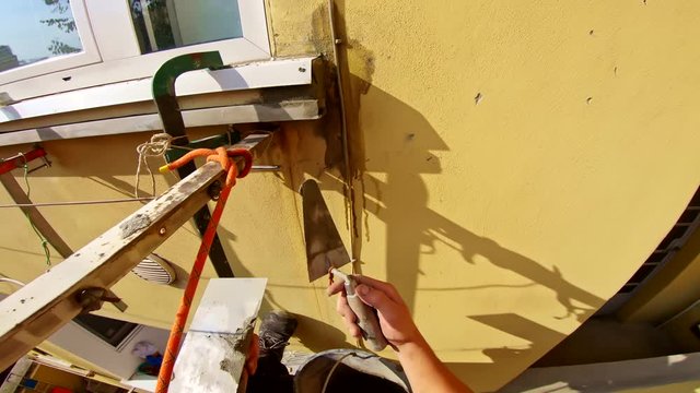 Abseiler workers with rope access and gear at building site, applying cement at home