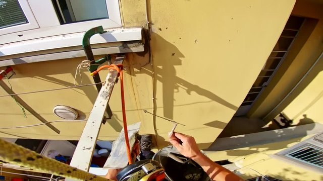 Construction home worker applying cement on wall in rope access gear, point of view