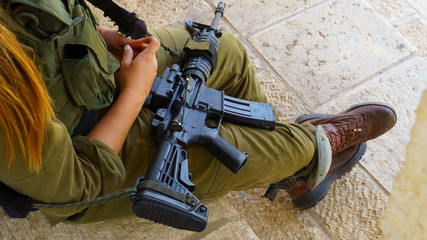 Israeli female soldier in green uniform sitting with a gun in her lap