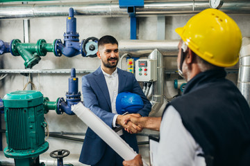 middle aged industry worker and businessman handshake indoor in heating plant