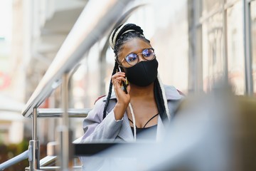 young pretty african american women in a medical protective mask outside in cafe. african girl with tablet and phone.