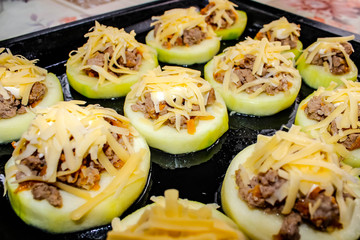 Raw zucchini on a baking sheet cut into rings, stuffed with minced meat and cheese.