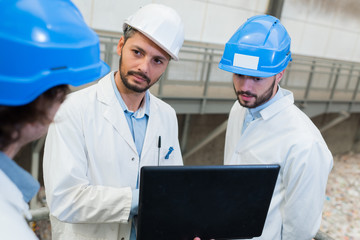 men in labcoat with hardhat on and laptop