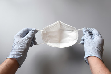 the doctor's hands protected by blue gloves hold a white ffp2 mask on gray background, against...