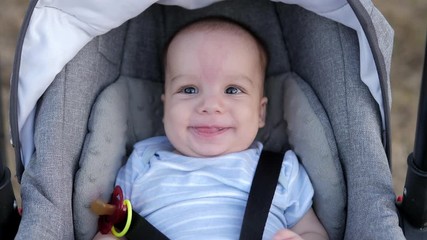 Happy baby in modern stroller in car seat. Summer park