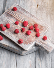 Raspberry fruits on old cutting board, healthy pile of summer berries on grey wooden background, angle view