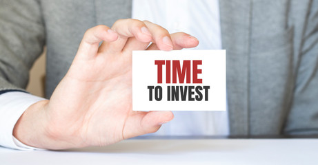 Businessman holding a card with text TIME TO INVEST, business concept