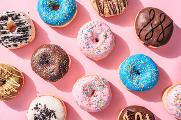 Various colorful donuts on top of pink background. High point view.