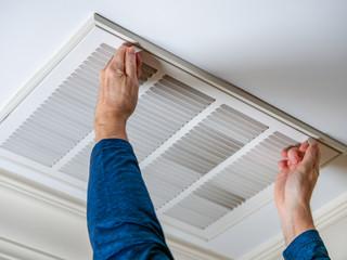 Man opening ceiling air vent to replace dirty HVAC air filter. Home air duct system maintenance for clean air.