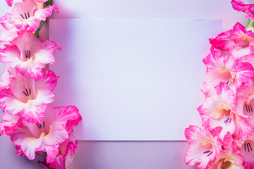 Empty white gift card, surrounded with gladiolus flowers, on top of purple background.