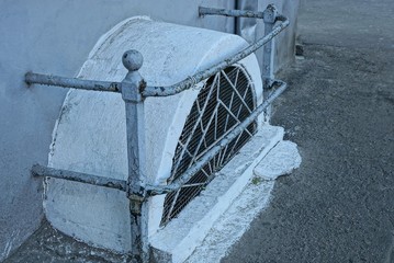 white old concrete basement window with iron grating on gray asphalt near the wall of the building