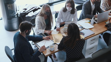 Top view happy multiethnic creative start-up business people wear masks working at meeting at light modern office table.