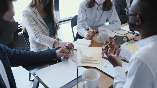 Close-up Young Diverse Business People Wearing Masks Against COVID-19 Working At Meeting At Light Modern Office Table.