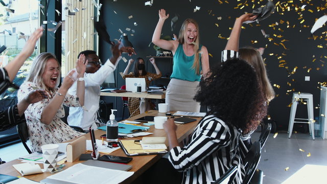 COVID-19 is over. Happy multiethnic business people team take masks off, celebrate normal life with confetti at office.