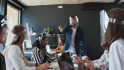Safety at workplace during coronavirus. Happy young male boss leading multiethnic business people team office meeting.