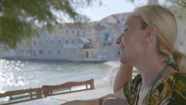 A young woman enjoys the shade under the trees next to the beach on the Adriatic Sea. She feels relieved and enjoys the moment. The end of the corona virus pandemic.
