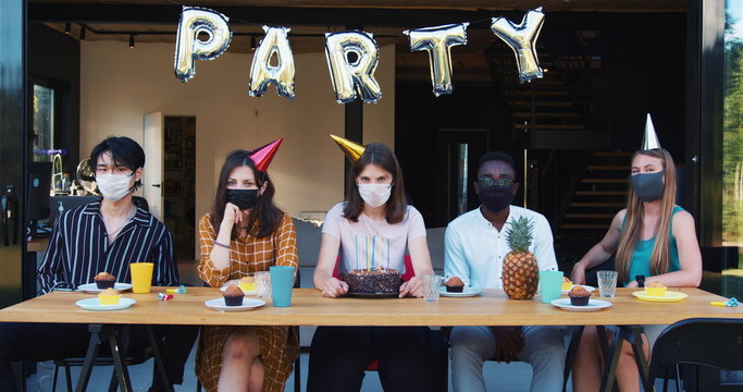 Party after COVID-19. Young upset sad multiethnic friends in masks feeling wrong at birthday celebration slow motion.