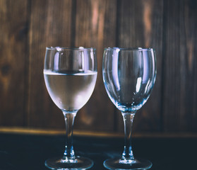 Two glasses of wine stand side by side on a wooden background, one glass of water the other an empty glass